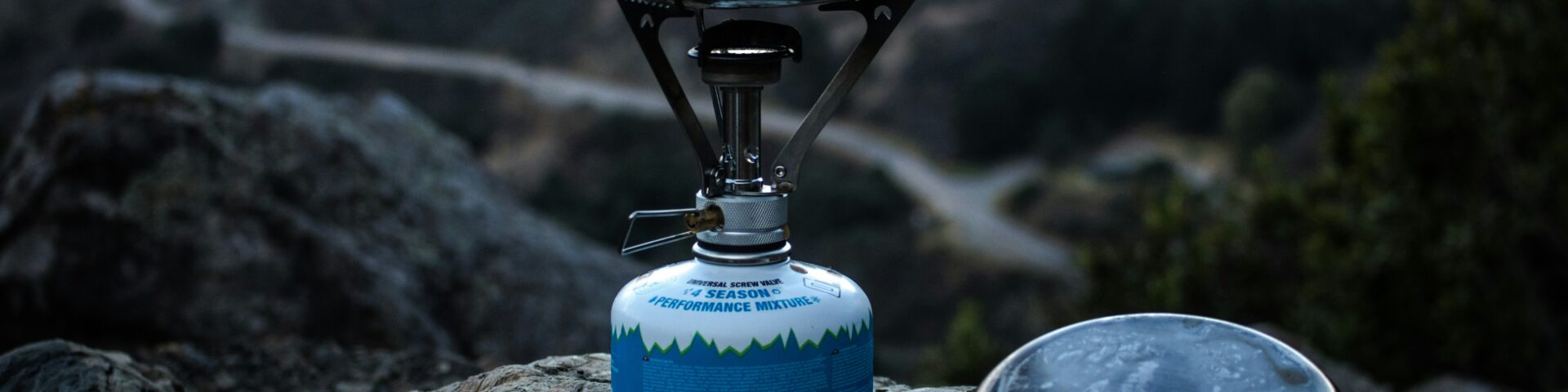 selective focus of blue and gray camping gas burner and cooking pan on cliff